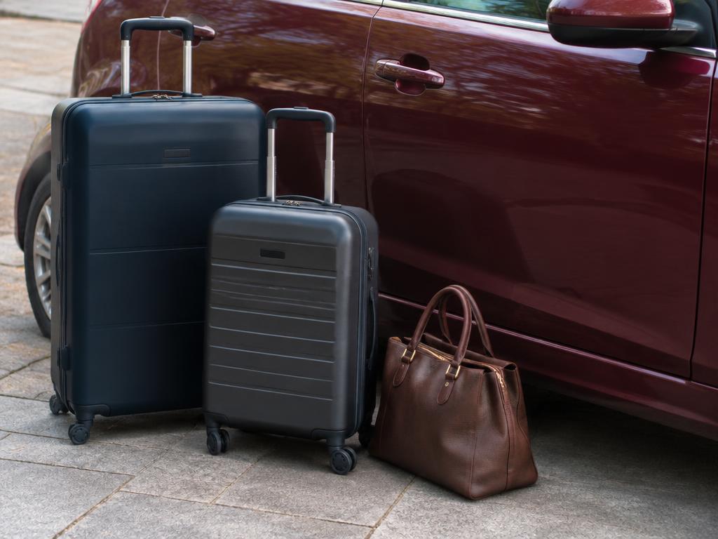 Una maleta grande, una maleta de cabina y un bolso de mano junto a un automóvil vino tinto